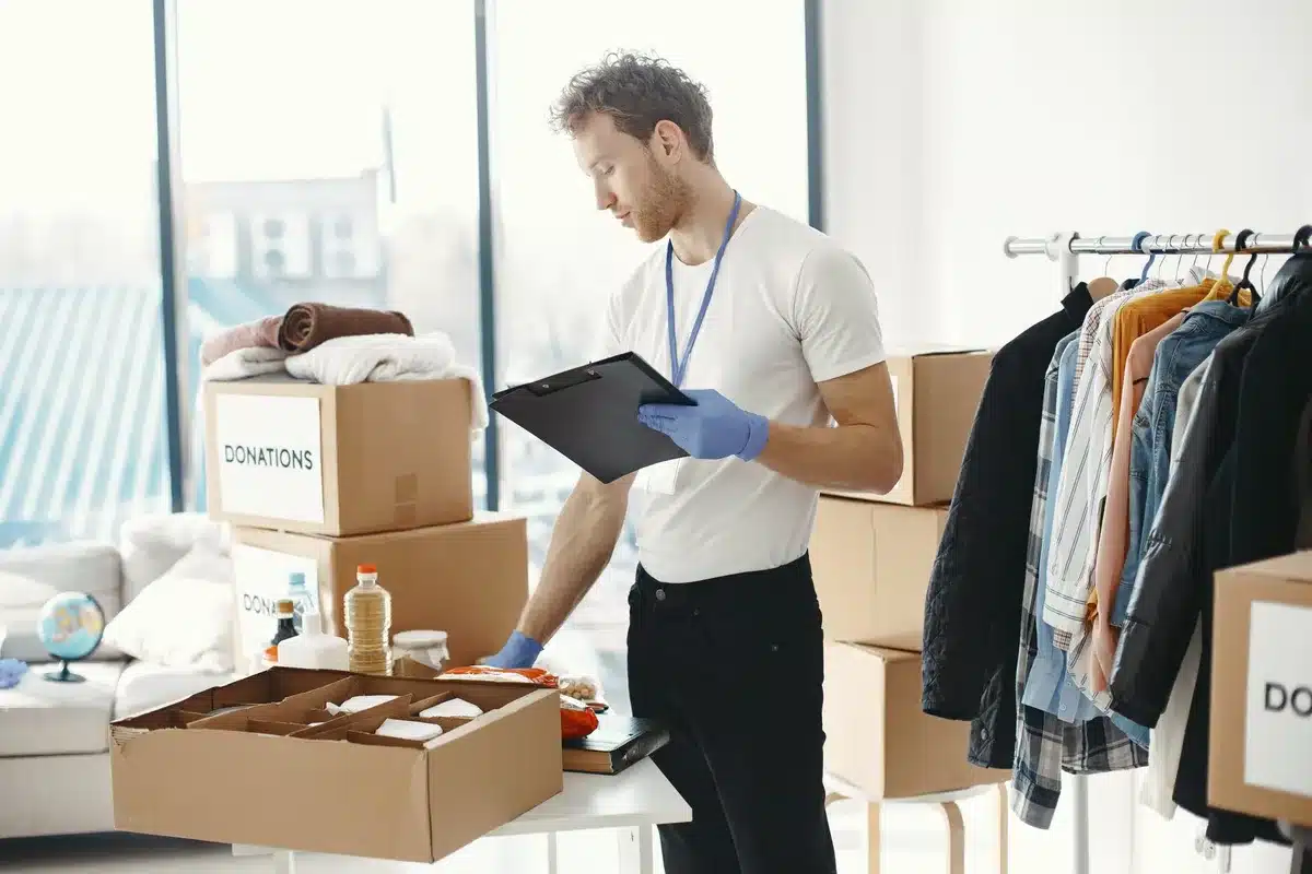 Mains triant des vêtements usés près de bacs de recyclage et de dons