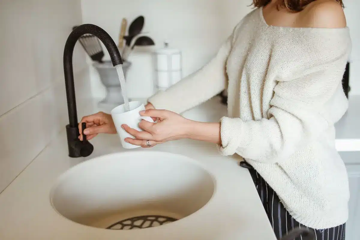 Une personne verse de l'eau dans un verre à la cuisine