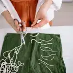Mains assemblant des chemins de table colorés sur une surface plane pour créer un tapis artisanal
