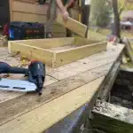 Réparation d'un trou dans un porche en bois avec du mastic et une spatule