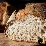 Pain au levain rustique déchiré en morceaux sur une surface en bois, avec un pain classique à côté