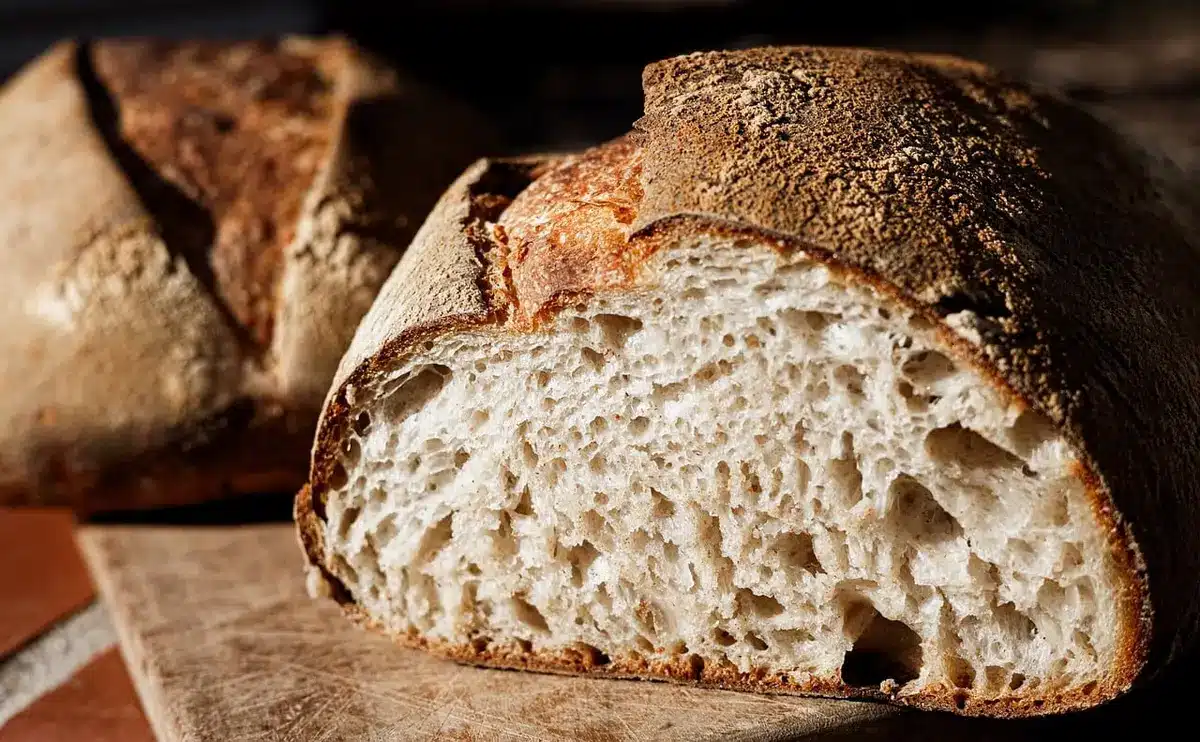 Pain au levain rustique déchiré en morceaux sur une surface en bois, avec un pain classique à côté