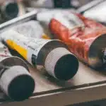 Atelier en plein jour avec bouchons en plastique, mains gantées et pots de peinture sur un établi