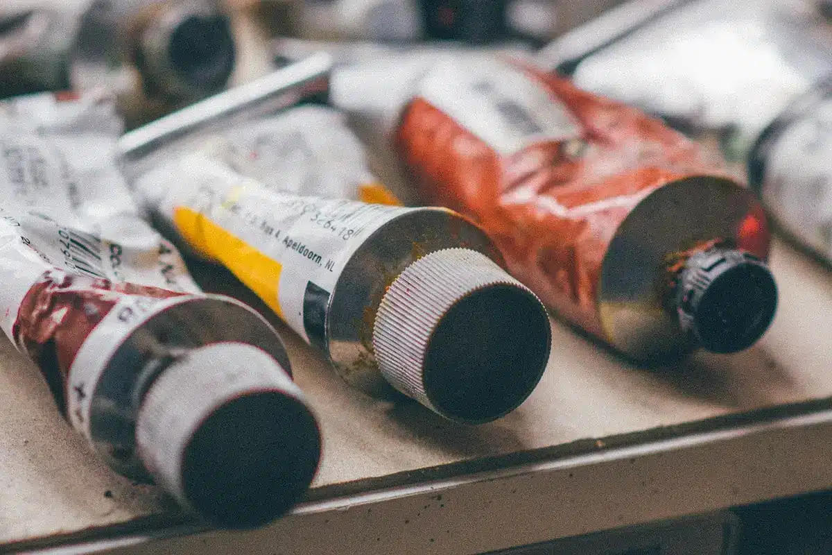 Atelier en plein jour avec bouchons en plastique, mains gantées et pots de peinture sur un établi