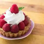 Tourte aux courges dorée sur une table rustique près d'une fenêtre, mains coupant une part