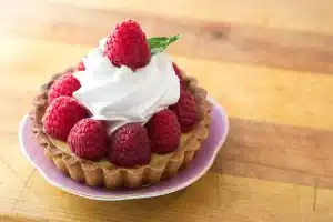 Tourte aux courges dorée sur une table rustique près d'une fenêtre, mains coupant une part